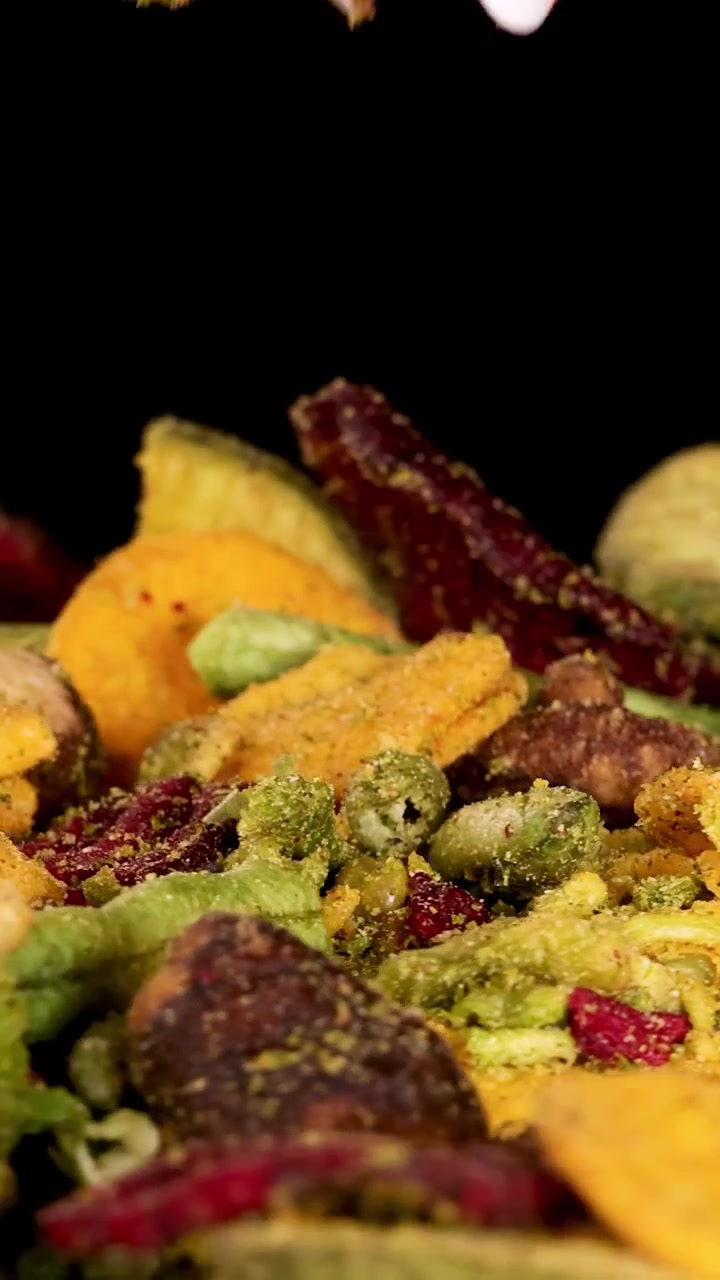 Una mano raccoglie patatine di verdure essiccate croccanti assortite, tra cui barbabietola, patata, fungo e fagioli, sotto una luminosa illuminazione da studio con uno sfondo nero