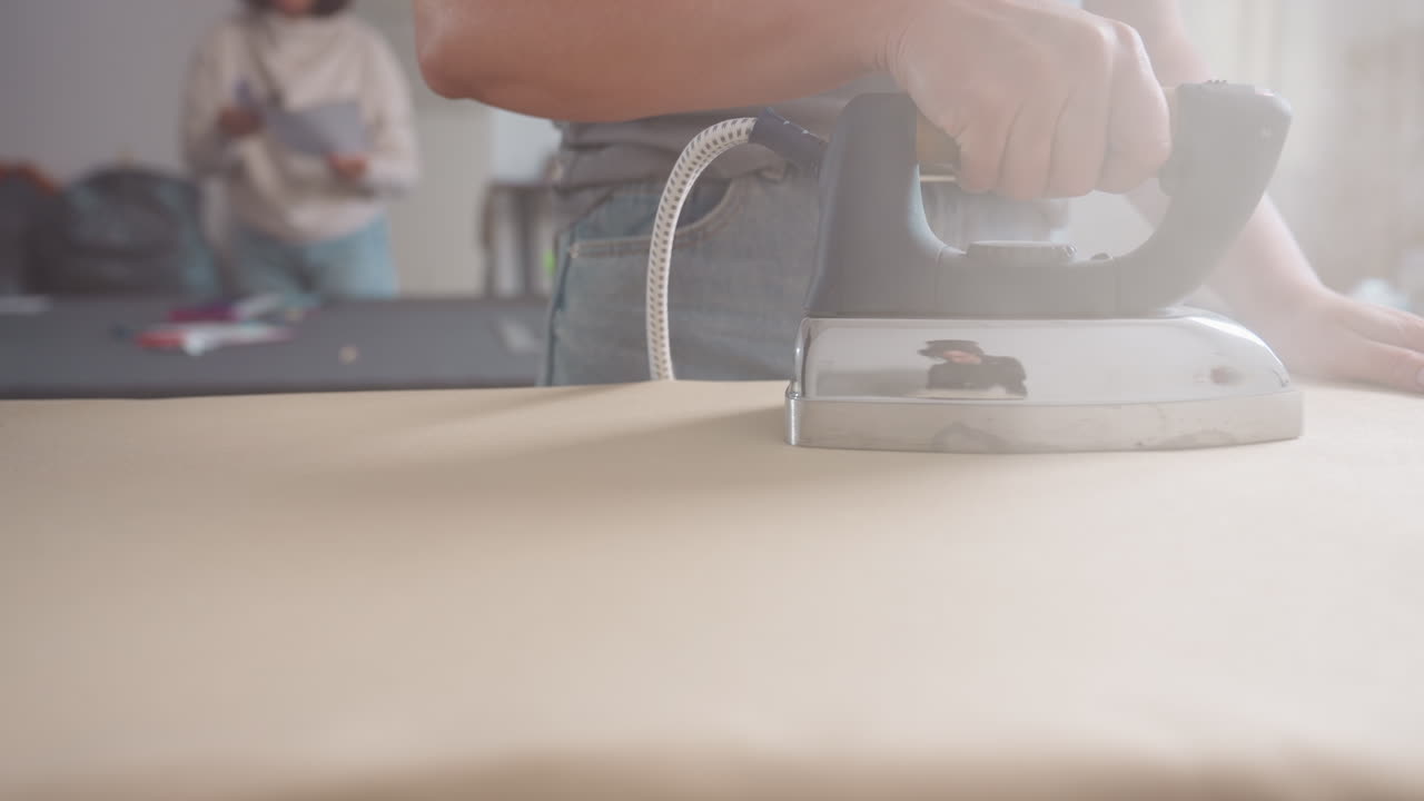 Close up of creative person ironing, steam rising from iron, focusing on crisp finish, skillful approach, ensuring professional garment result, highlighting artistry, bright workspace synergy