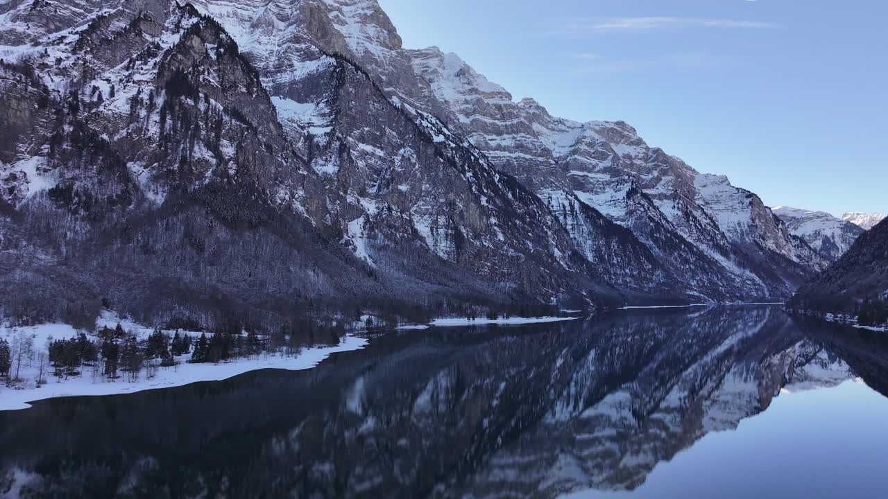 Symmetrical beauty of water intake at Klöntalersee, reflecting snow clad Swiss alps in winter serenity, breathtaking aerial view.