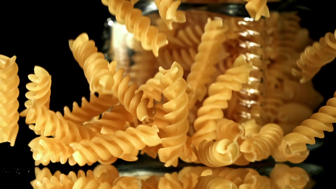 Pasta fusilli cruda che cade su una superficie riflettente al rallentatore.