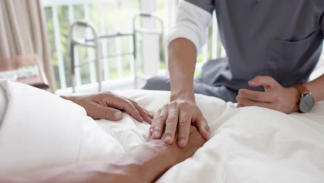 mid section of diverse male doctor discussing with senior male patient in bed at home, slow motion