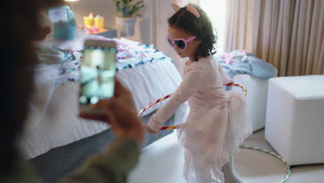 Fröhliches-Kleines-Mädchen,-Das-Im-Schlafzimmer-Mit-Hula-Hoop-Reifen-Tanzt.-Mutter-Fotografiert-Mit-Smartphone-Und-Teilt-Es-In-Sozialen-Medien