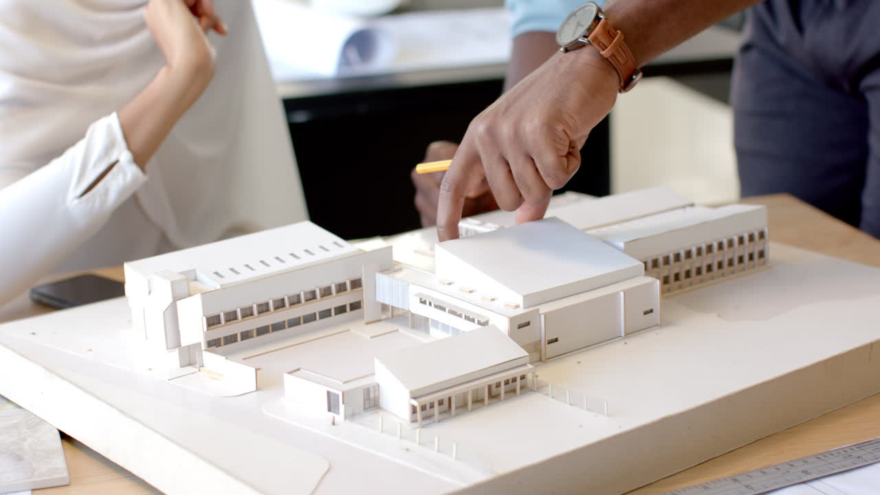 Pointing at architectural model, business professionals discussing project details in office