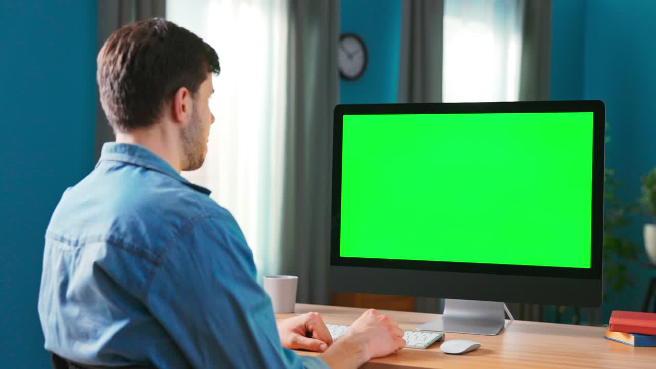 쾌적한 거실에서 책상에 앉아있는 동안 녹색 모의 화면을 가진 현대적인 컴퓨터를 사용하는 남자의 클로즈업. 예쁜 남자는 가족, 의사, 금융 고문과 비디오 채팅을합니다.