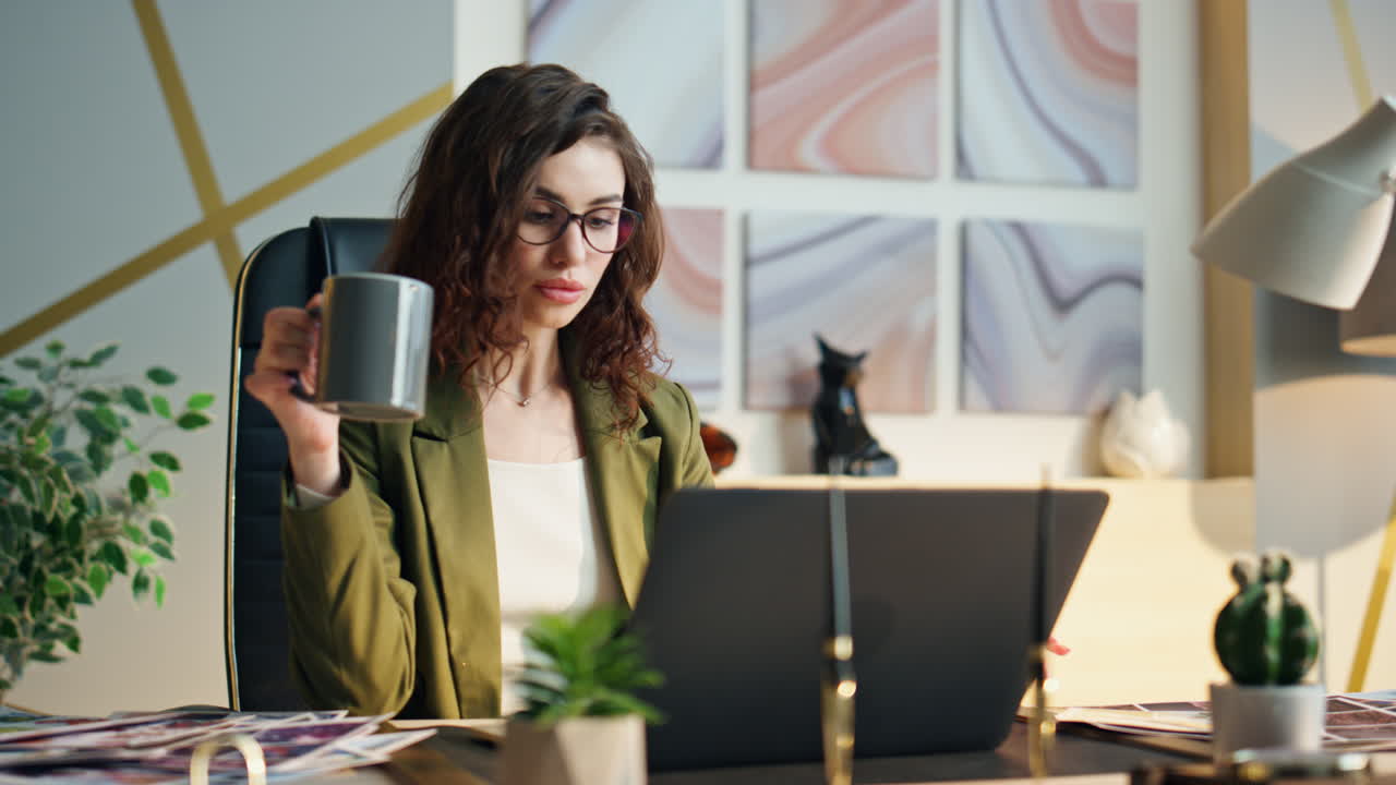 Giovane manager seria beve caffè seduta in un moderno ufficio, primo piano.