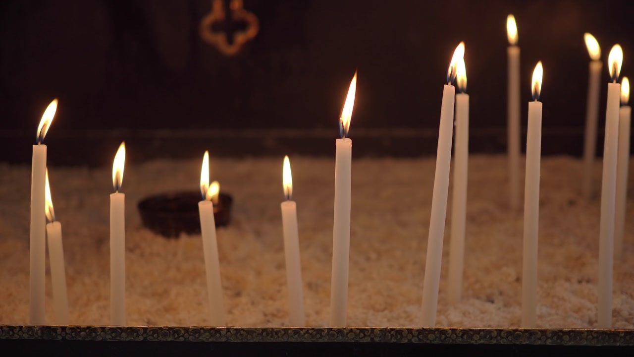 Multiple White Candles Burning and Flickering in a Dark Church