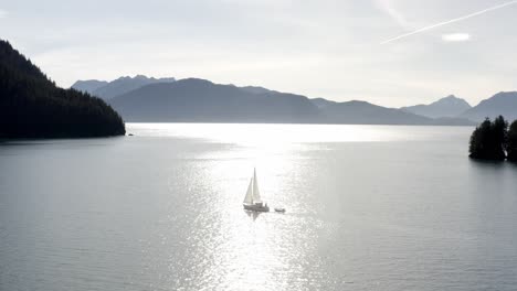 small boat next to luxury yacht sailing on calm ocean water illuminated by sunlight with mountain silhouette at background in alaska, usa