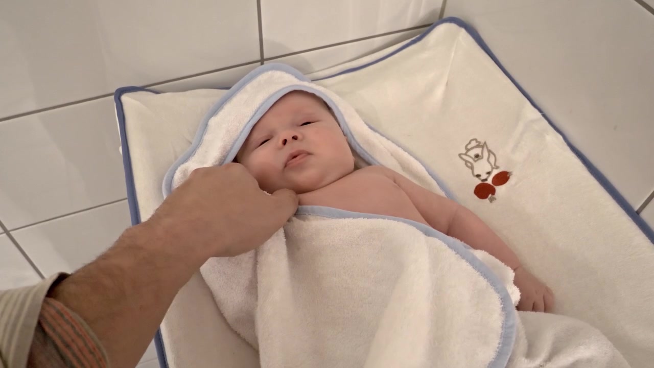 Neonato felice avvolto in un asciugamano. Mani del padre che accarezzano con tenerezza.
