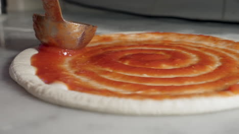 tomato sauce being spread onto pizza base in a swirling motion, close up shot