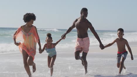 smiling african american family holding hands and running on sunny beach