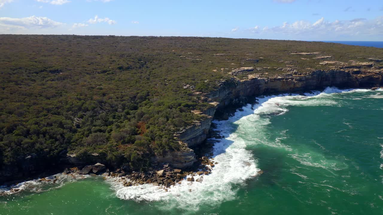 las olas rompen a través de los acantilados costeros de arenisca con una exuberante vegetación en el parque nacional real en sydney, nueva gales del sur, australia