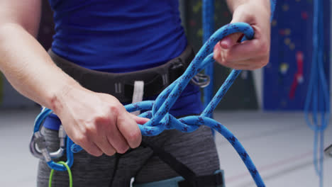 Mittelteil-Einer-Kaukasischen-Frau,-Die-An-Einer-Indoor-Kletterwand-Ein-Seil-In-Einem-Klettergurt-Sichert