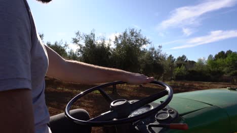 Farmer-driving-tractor-in-olive-fields,-detail-of-hand-behind-the-wheel