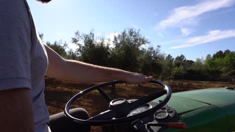 Granjero-Conduciendo-Tractor-En-Campos-De-Olivos,-Detalle-De-La-Mano-Detrás-Del-Volante