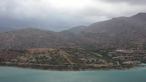 aerial tour with the drone as it flies towards the small mountains, capturing the cityscape in the background and the road where cars drive along the coast