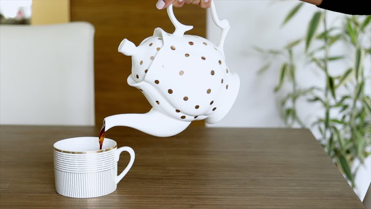 Vertiendo té a mano desde una tetera de lunares en una taza de té