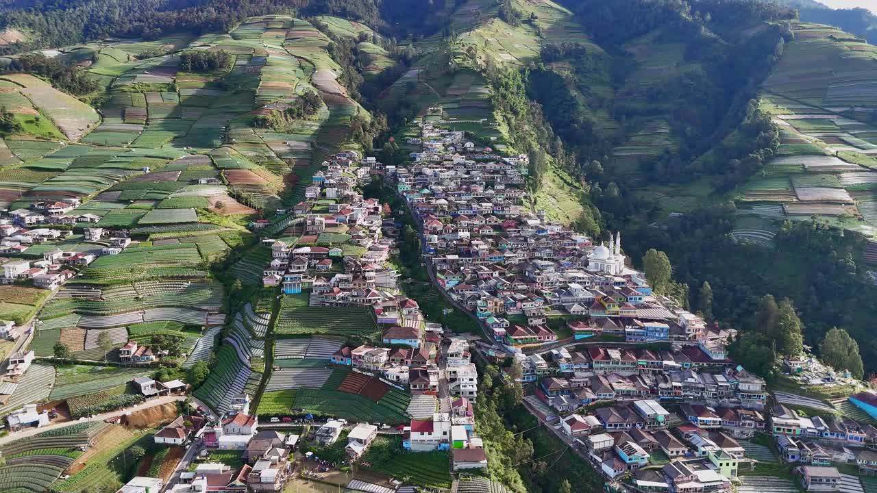 Beautiful drone view of rural Indonesian village with traditional houses surrounded by green terraced farmland on mountain slope. Nepal Van Java, Mount Sumbing, Indonesia