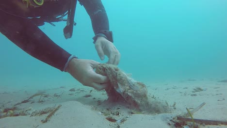 a scuba diver removes rubbish buried in the sand on the ocean floor