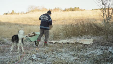 un hombre está empleando cartón como mantillo, con su perro a su lado - toma estática