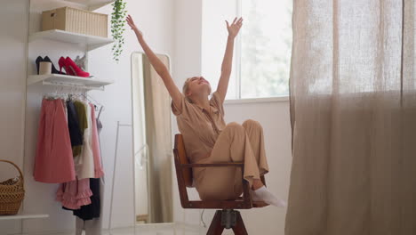 happy woman spins on chair putting hands up in fitting room