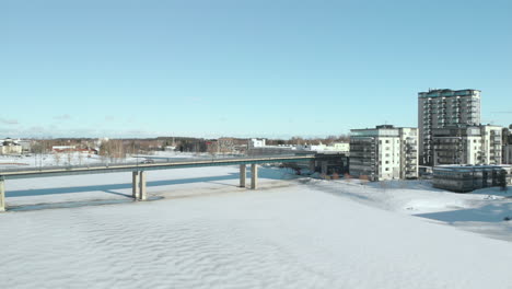 aéreo, marcha atrás, toma de drones, panorámica sobre pielisjoki, lejos del tráfico en el puente suvantosilta y edificios de apartamentos, en la orilla del río en un día soleado de invierno, en joensuu, karelia del norte, finlandia