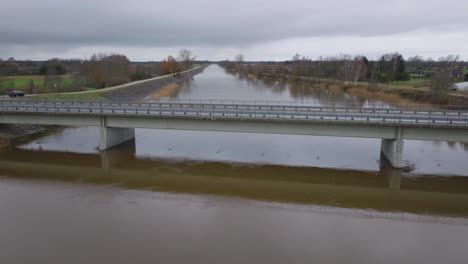 aerial establishing view of high water in springtime, barta river flood, brown and muddy water, overcast day, wide drone shot moving forward over the bridge