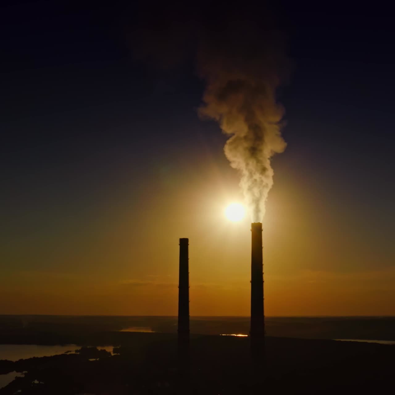 Smoke from manufacturing at darkness. Industrial pipes with chemical emissions on the setting sun background. Pollution the environment.