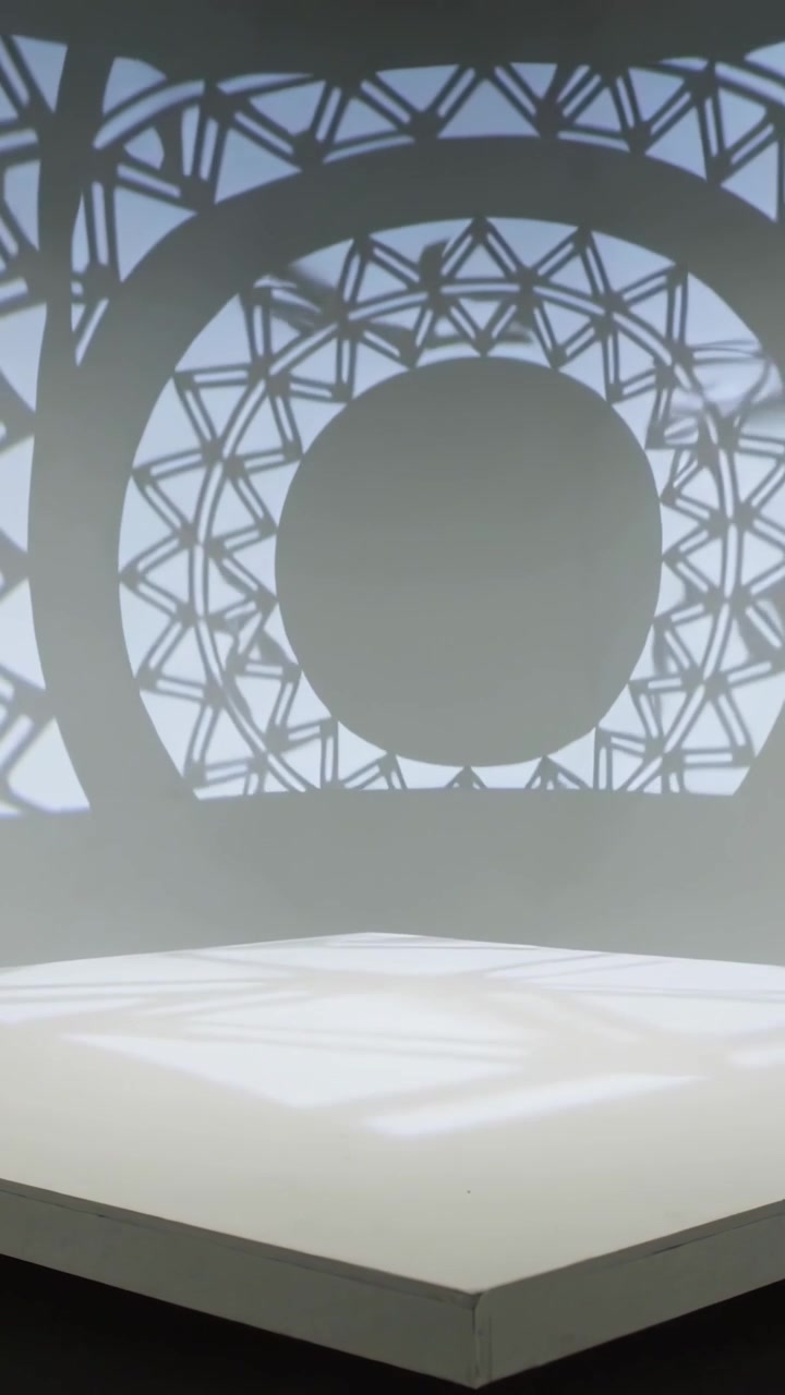 Video verticale: Luce che rivela un motivo geometrico attraverso l'angolo di una galleria, animando un piedistallo bianco.