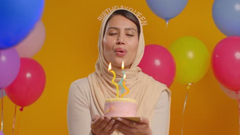 retrato de estudio de una mujer con hijab y cinta para la cabeza de la reina del cumpleaños celebrando el cumpleaños soplando velas en el pastel