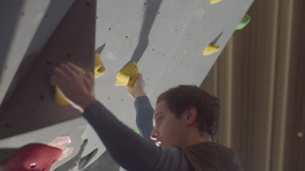 disparo en ángulo bajo de un joven atleta escalando una pared de roca artificial en un gimnasio de boulder