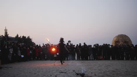 slow motion clip of a male stunt performer performing fire dance using torches on a spinning rod during fire festival on a beach in south korea at sunset.