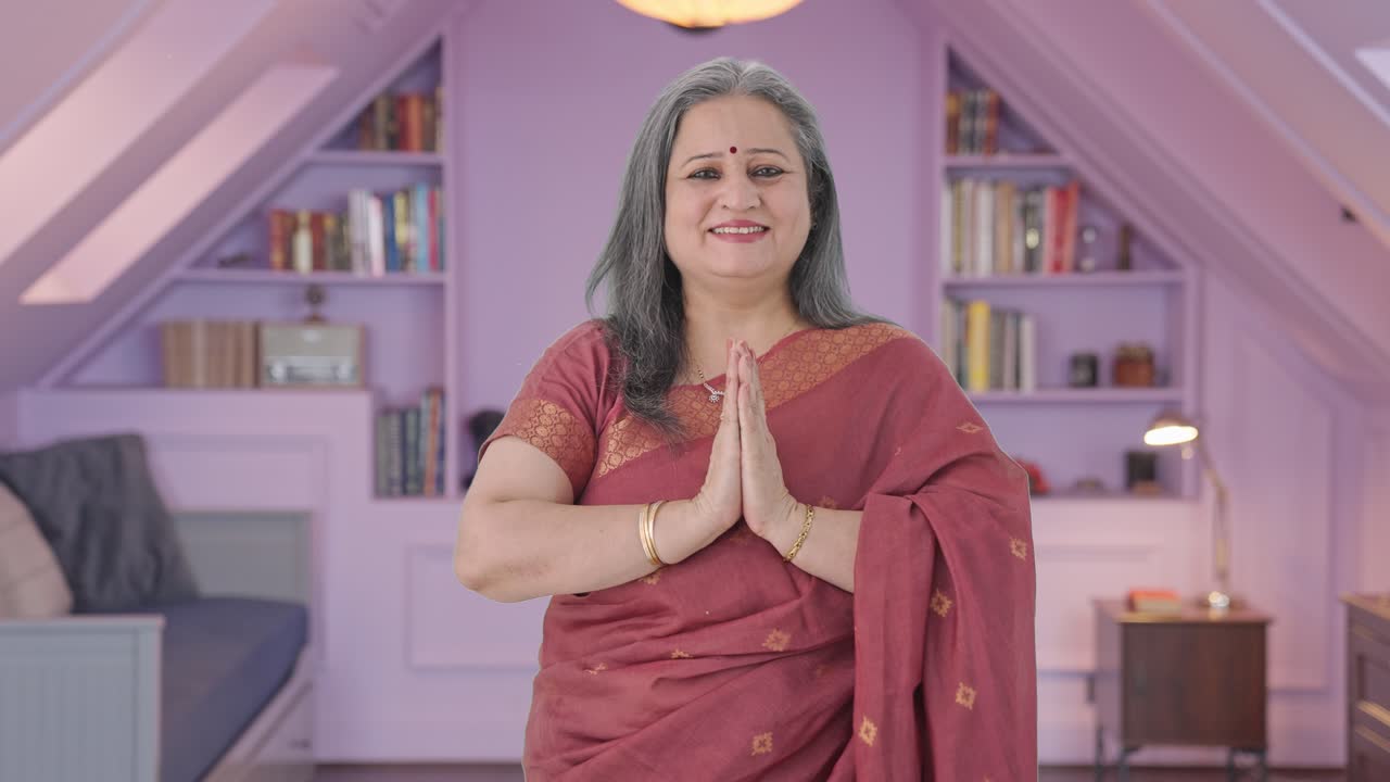 Glückliche indische alte Frau macht Namaste und begrüßt Gäste