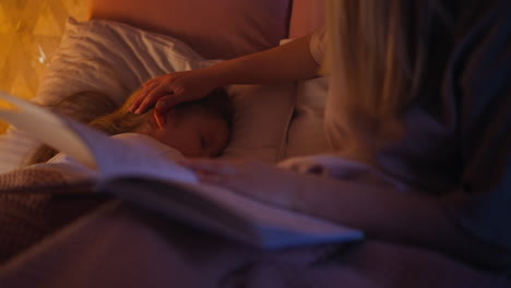 mother with book takes care of daughter sleeping on bed