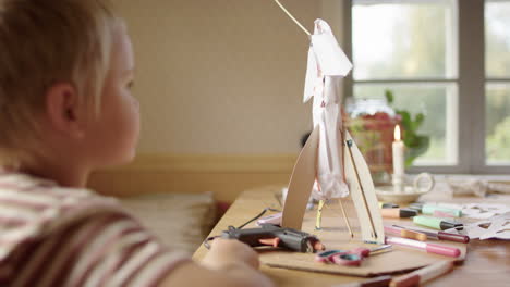 Young-caucasian-boy-admiring-his-paper-rocket-science-experiment-indoors