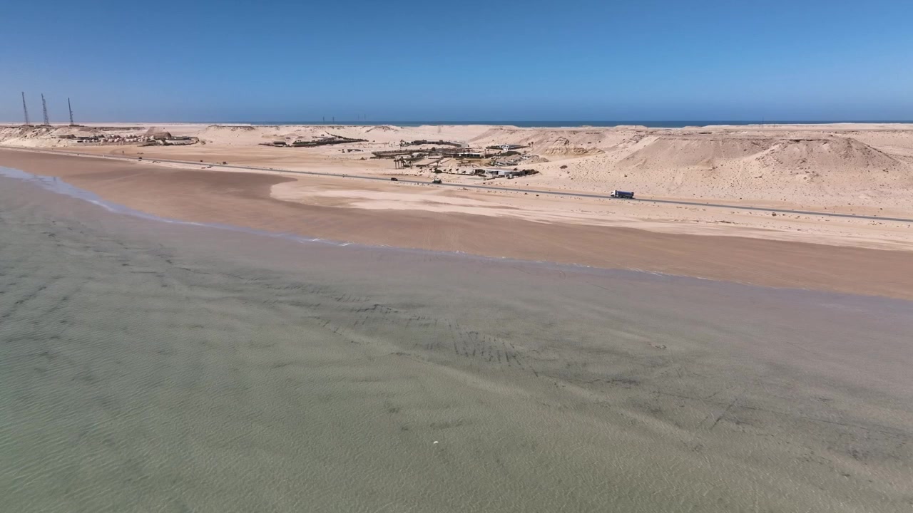 Drone luftfoto af lavt turkisblåt vand, der grænser op til ørkenkysterne ved Dakhla-bugten i det sydlige Marokko. Fredfyldt kystlandskab, der fremhæver den unikke overgang mellem hav og Sahara.