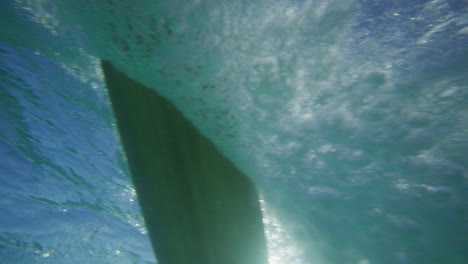 surfista montando en una ola en aguas cristalinas en la bahía de byron, australia, disparado desde debajo del agua en cámara lenta.