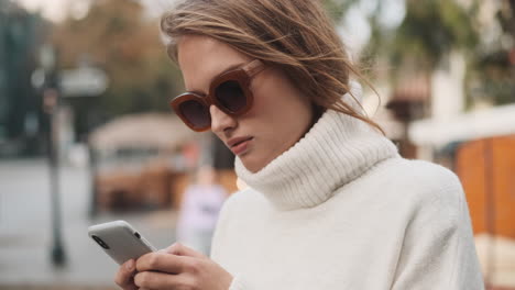 caucasian female in sunglasses using smartphone outdoors.