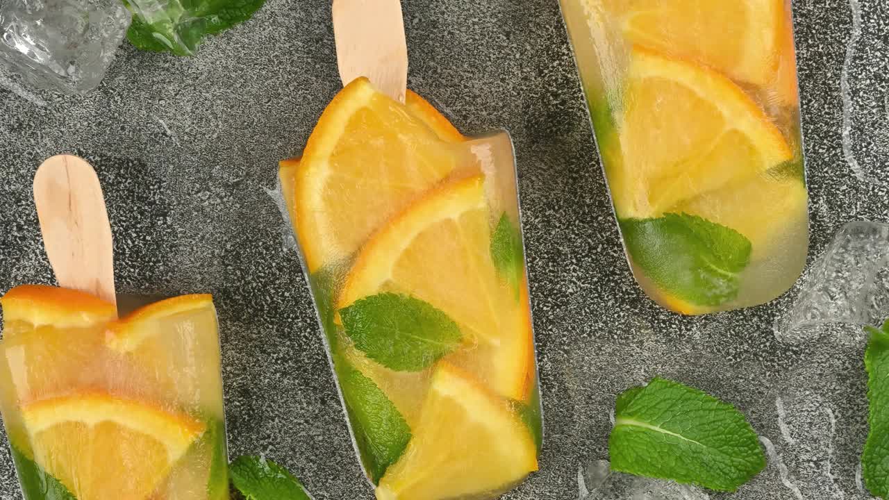 오렌지와 민트 아이스 팝시클이 테이블 위에 회전하고 있습니다.