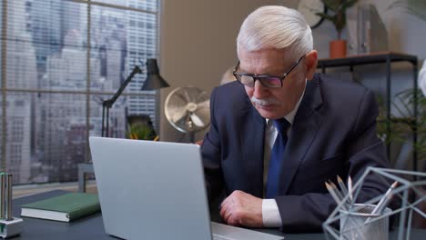 Concentrated-senior-business-man-using-laptop-sits-at-office-desk-workplace-web-designer-online-work