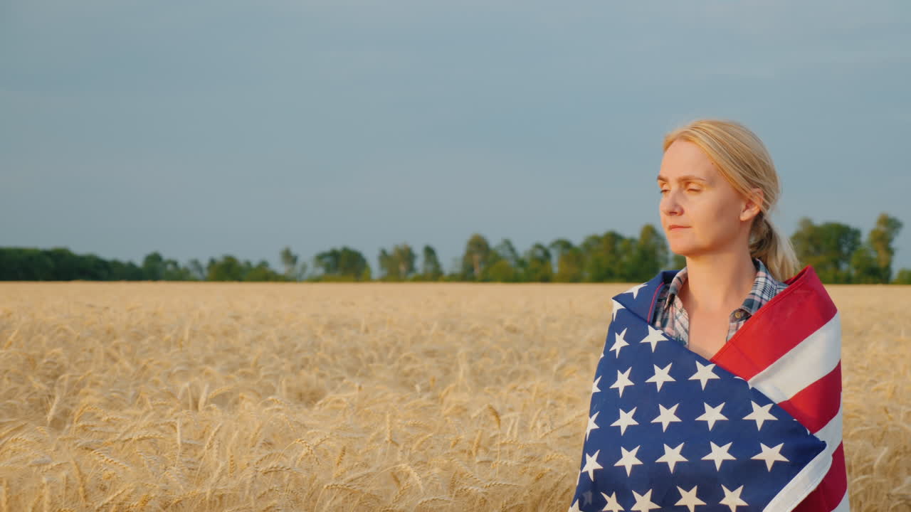 mujer agricultora con bandera de estados unidos sobre malezas caminando por el campo de trigo