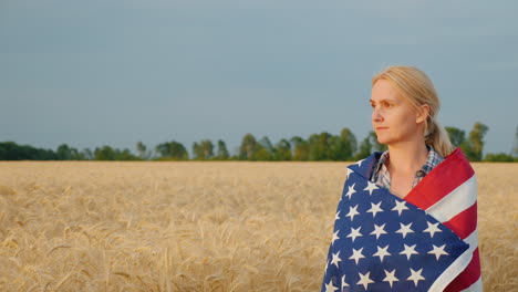 woman farmer with usa flag on weeds walking along wheat field