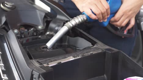 primer plano de manos sosteniendo una boquilla de combustible expulsando bencina a la cámara de combustible de motocicleta o scooter