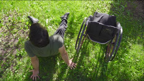 the physically disabled young man lies on the grass and leans against his wheelchair.