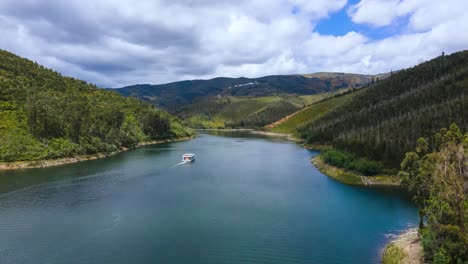 Lufthyperlapse-Eines-Bootes,-Das-An-Einem-Bewölkten,-Sonnigen-Tag-Durch-Einen-Fluss-Fährt,-Der-Von-Pinienwaldtälern-Umgeben-Ist