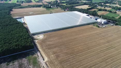 drone fly above a greenhouse with solar panel and sun shine reflection close to a plowed land field in a country side farming area in europe