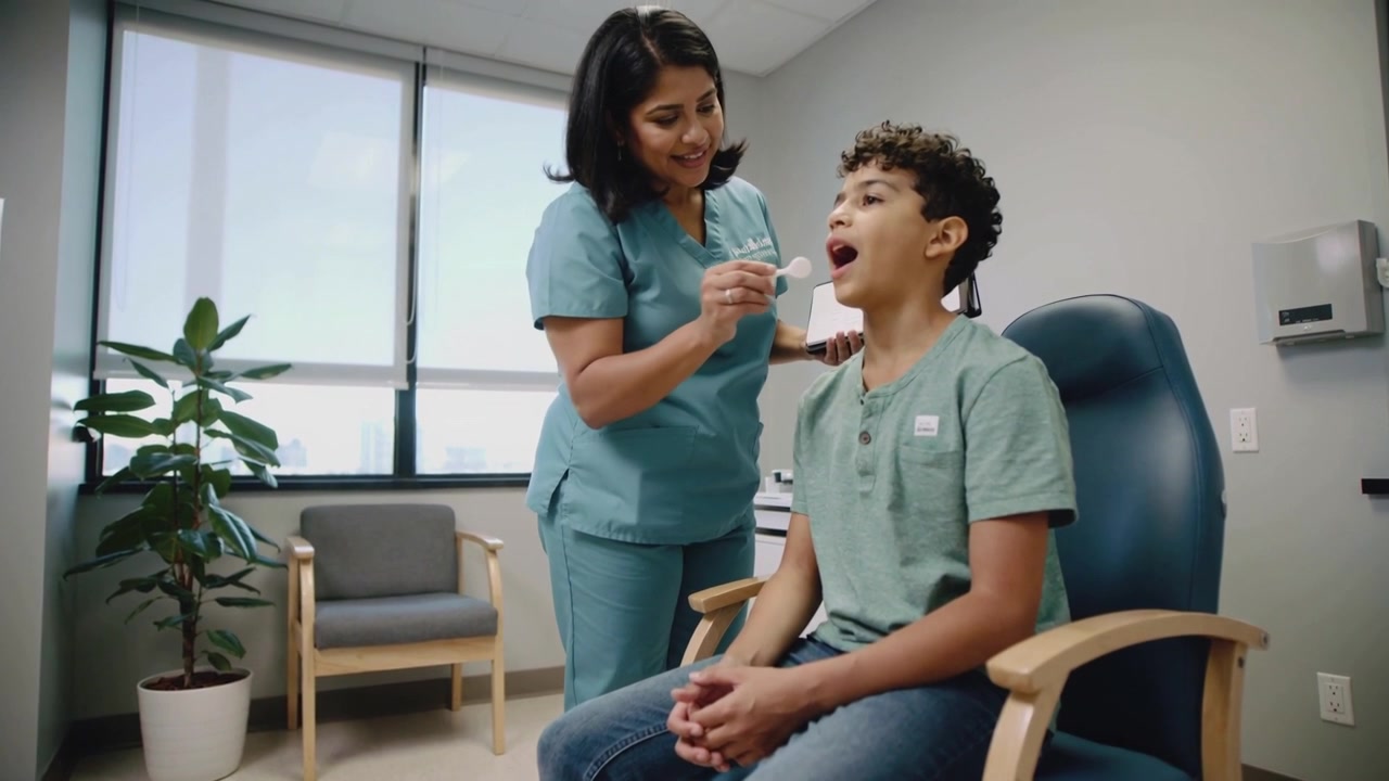 Positioning applicator, nurse in teal scrubs inspecting seated teen's mouth in clinic for exam