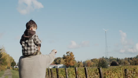 a farmer father shows his young son their wind turbine installed on a farm.