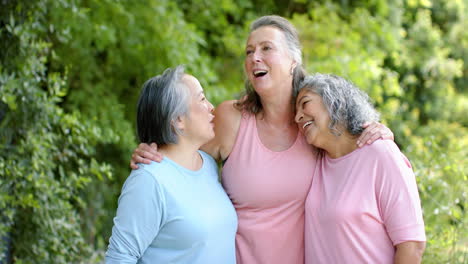 senior biracial woman embraces a caucasian woman and an asian woman outdoors