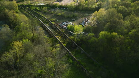 Ein-Schrottplatz-An-Den-Bahngleisen-In-Fayetteville,-Arkansas-Im-Frühling,-Viel-Grün-Drumherum,-Luftaufnahme