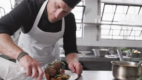 caucasian male chef cleaning plate with meal in kitchen, slow motion